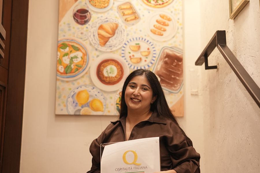 Chef Kamalika Anand with the plaque on the stairs beneath the painted table mural