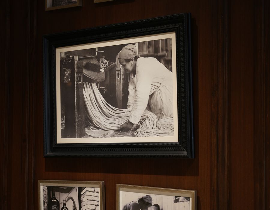 A framed photograph of a pasta maker at work, hung on dark wood
