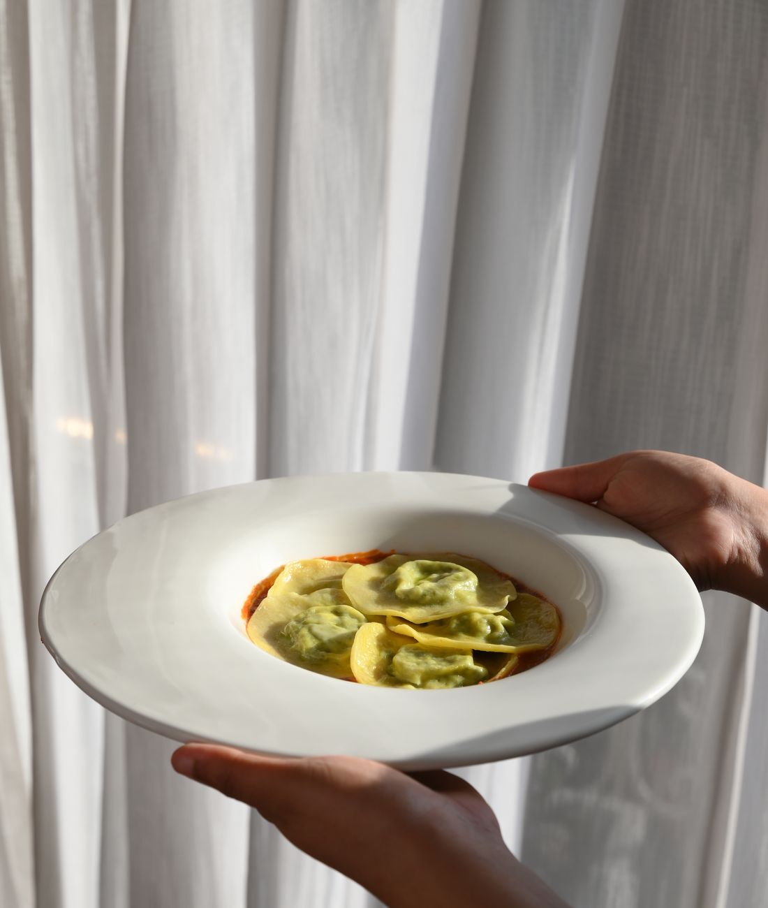 A plate carried to the table against a curtain of daylight